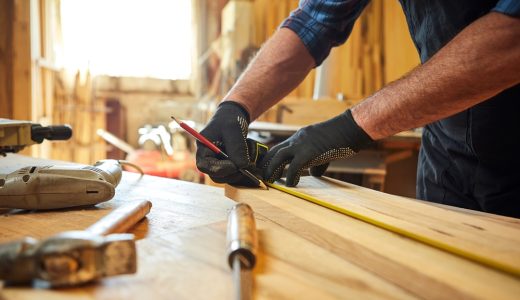 Carpenter working with a wood, marking plank with a pencil and taking measurements to cut a piece of wood to make a piece of furniture in a carpentry workshop, close-up view