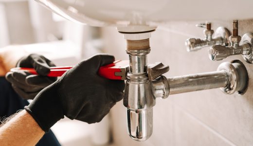 Plumber in black gloves fixes a sink pipe with a wrench in a bathroom, showcasing precision and craftsmanship